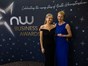 Two people in formal wear, one wearing a black dress and one wearing a dark blue dress, standing in front of a dark blue background with writing "NW Business Awards"