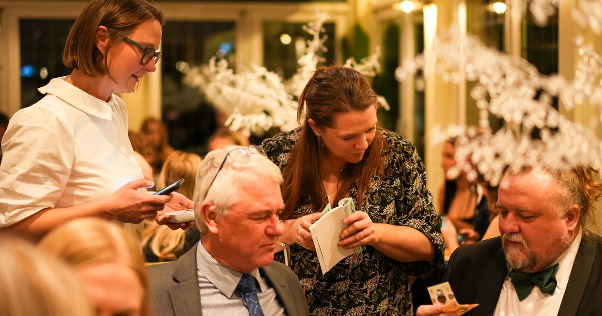 male guests wearing suits are sat at dining tables talking with females who are standing