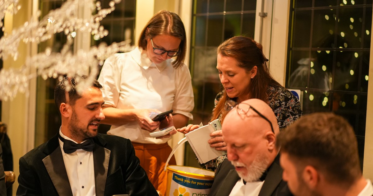male guests wearing suits are sat at dining tables talking with females who are standing