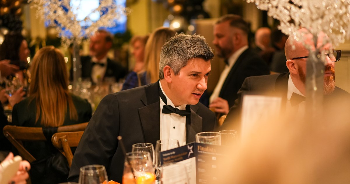 male guest wearing a black tie evening suit sat at dining table talking with other award evening attendees
